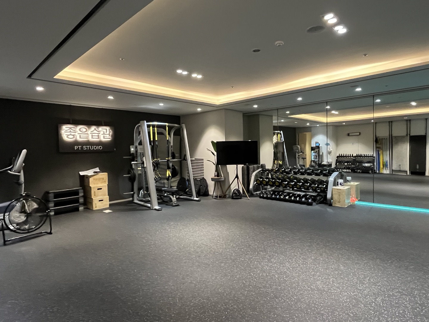 운동존. 좋은습관 PT STUDIO 사인 아래 스미스머신과 덤벨 랙이 놓여 있고 벽 한 면이 거울입니다.