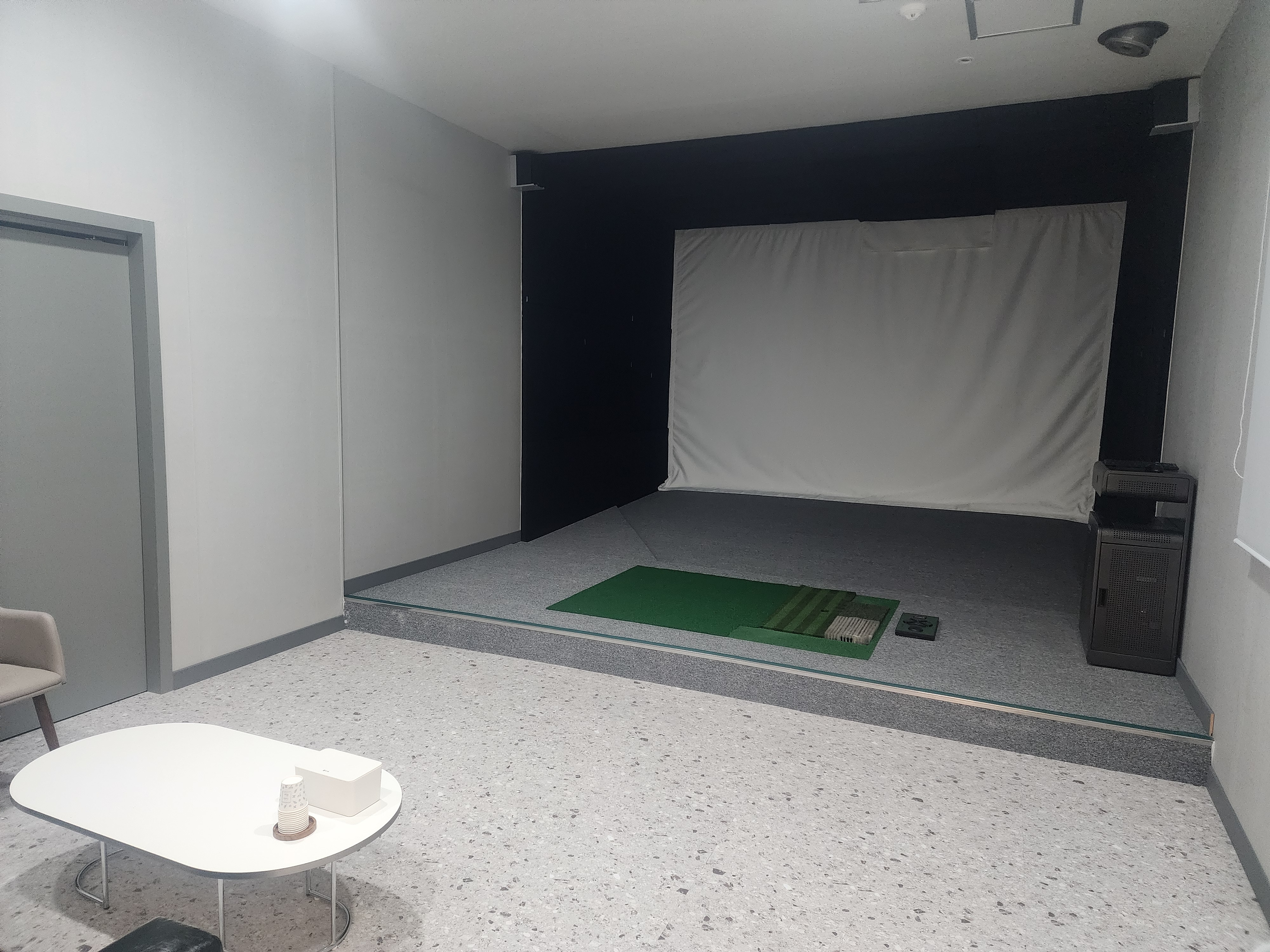 스크린 룸 내부. 스크린과 타석 매트, 기기 한 대가 있고 옆에 대기 테이블이 놓여 있습니다.