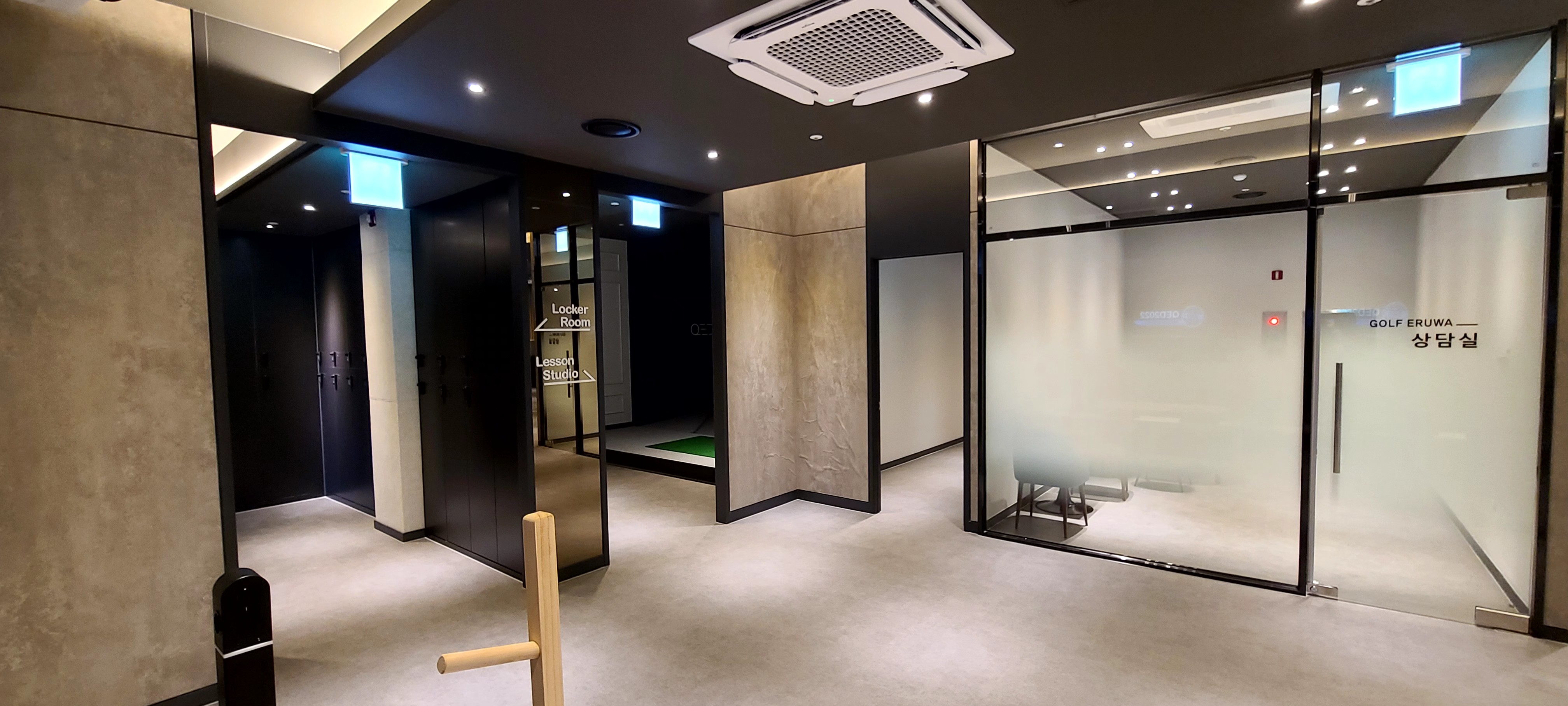복도. 천장에 Locker Room 과 Lesson Studio 방향 안내가 걸려 있고 오른쪽에 GOLF ERUWA 상담실 유리문이 있습니다.