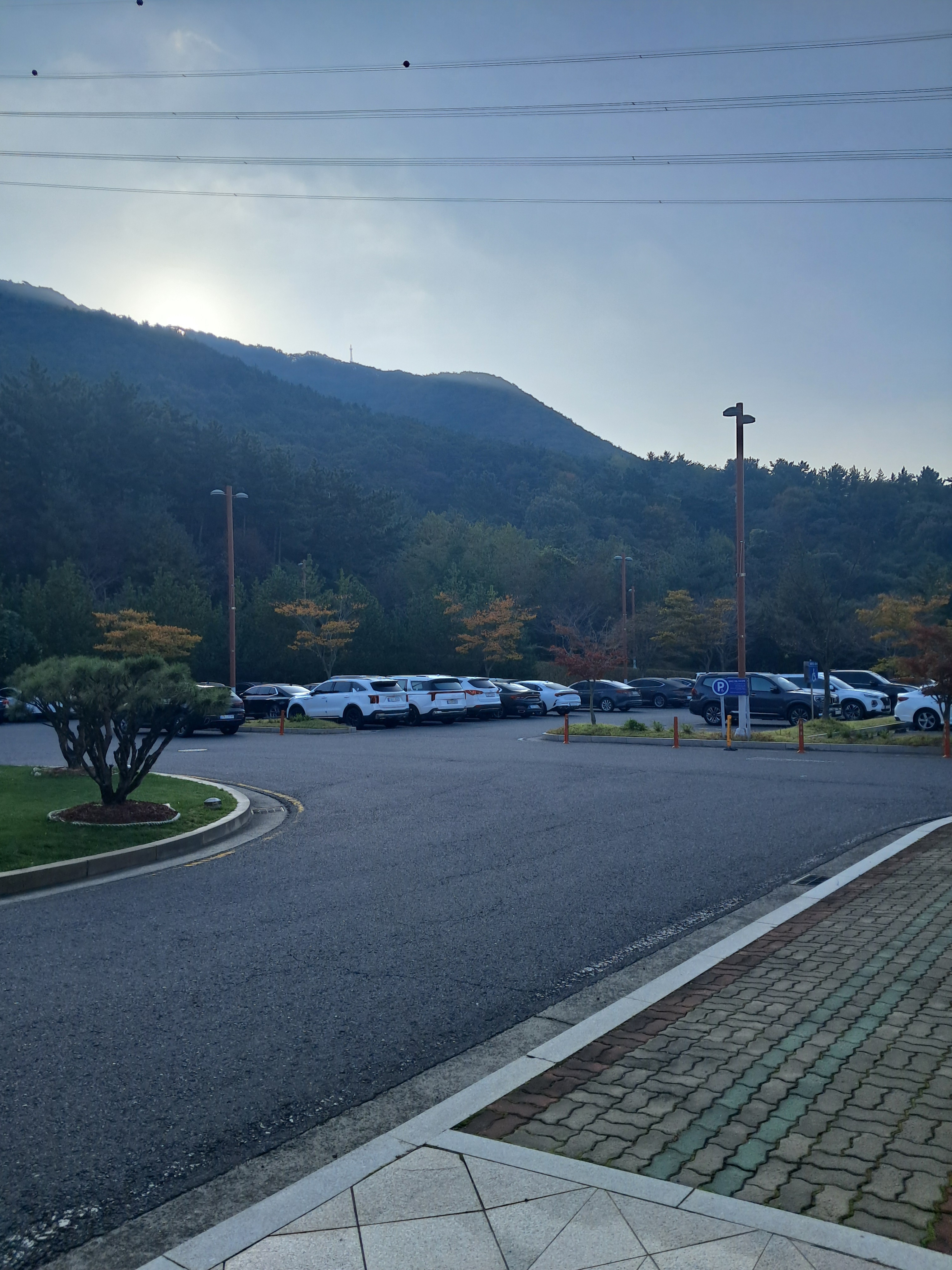 클럽하우스 앞 주차장. 넓은 주차 구역 너머로 산이 보입니다.