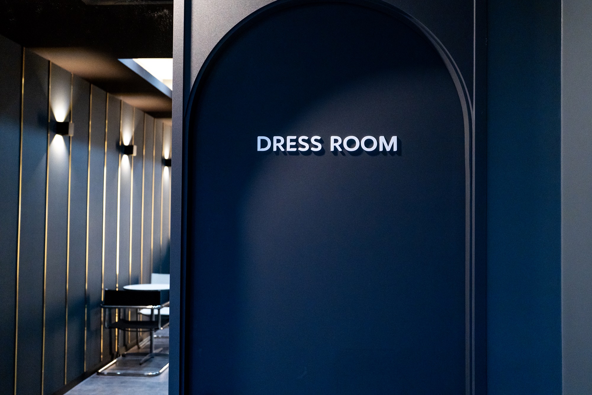 복도 끝에 DRESS ROOM 사인이 붙어 있고 옆으로 대기 테이블이 놓여 있습니다.