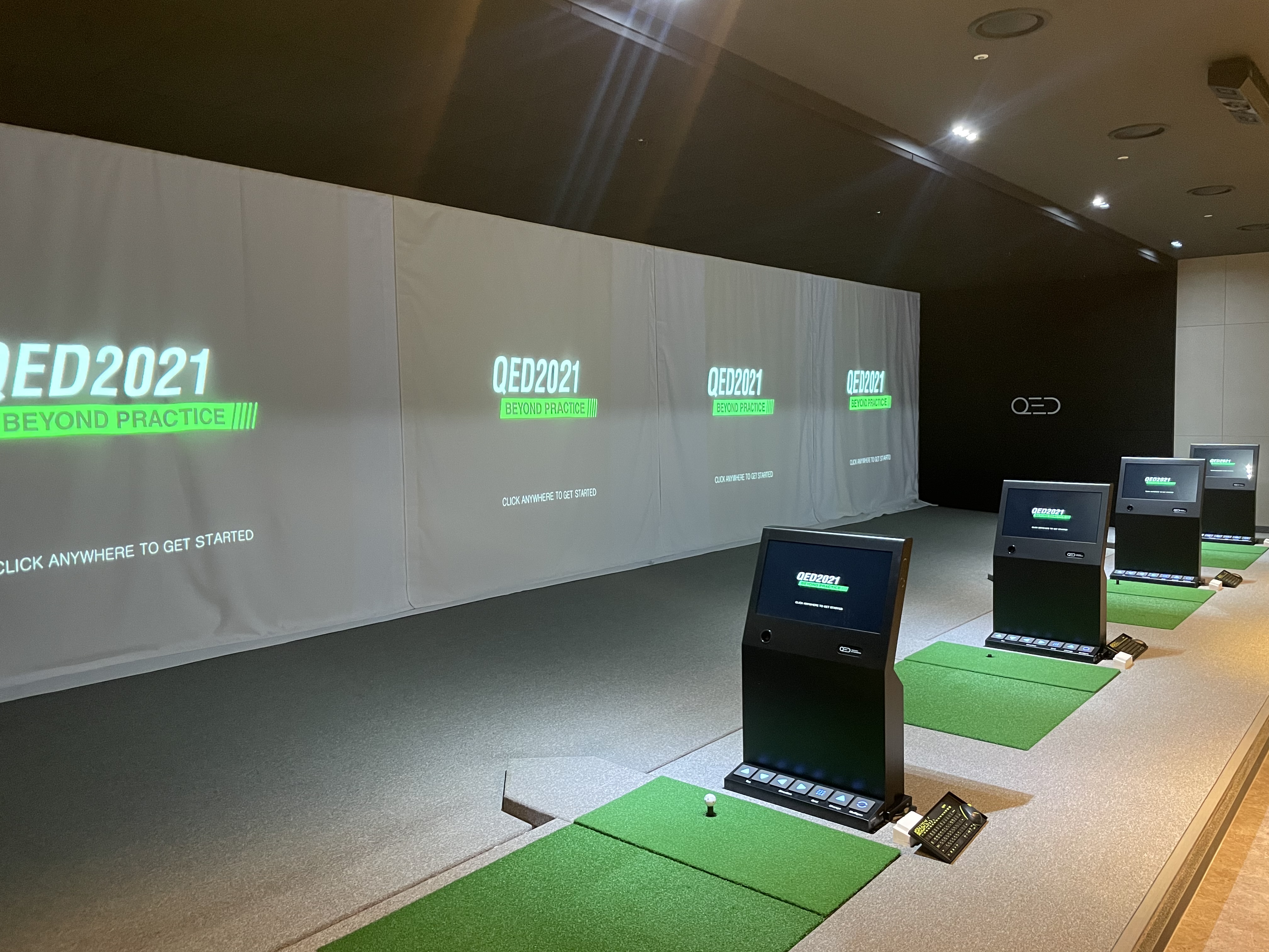타석열. 스크린마다 QED2021 BEYOND PRACTICE 와 CLICK ANYWHERE TO GET STARTED 가 떠 있고 타석마다 단말이 서 있습니다.