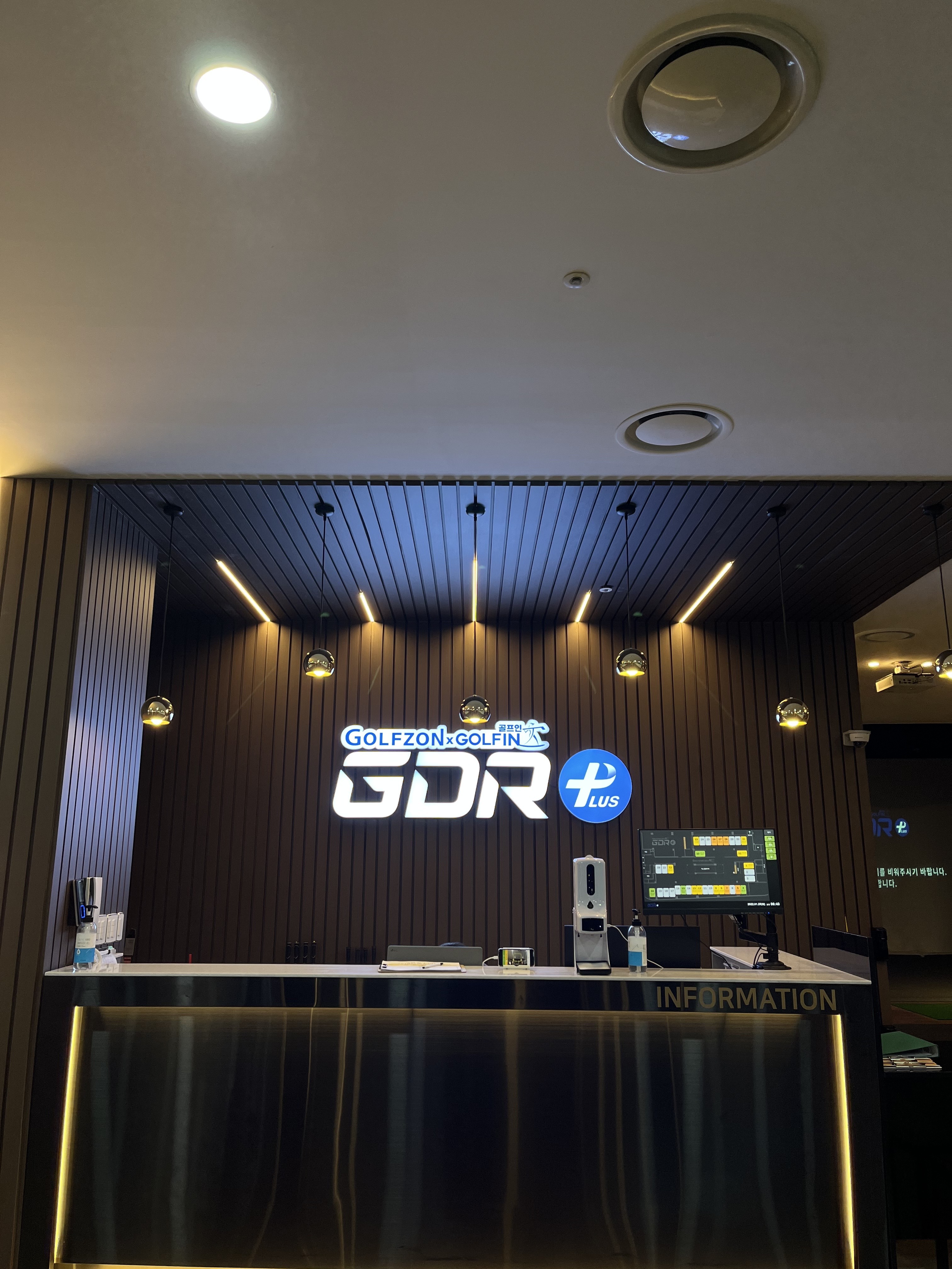 인포데스크. GOLFZON GOLFIN GDR PLUS 사인 아래 카운터가 있고 오른쪽에 타석 현황판 모니터가 놓여 있습니다.